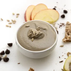 White bowl of brown sunflower seed butter next to apples and crackers.