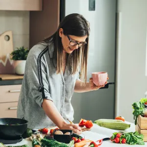 A woman writing down a recipe while in the kitchen and a lot of produce is on the counter.