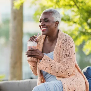 A Black Woman Enjoys a Smoothie on a Bench Outside