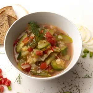 Bowl of zucchini creole with toast and onion, pepper, and herb garnishes