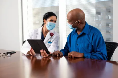 A Doctor Speaks to Her Patient in an Exam Room While Going Over His Charts on a Laptop.