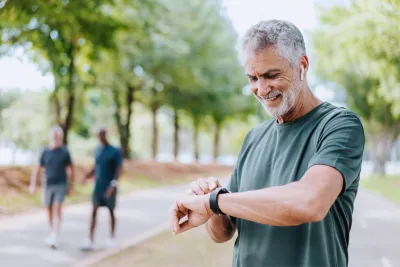 A Senior Man Checks His Smart Watch as he Takes a Break from His Walk