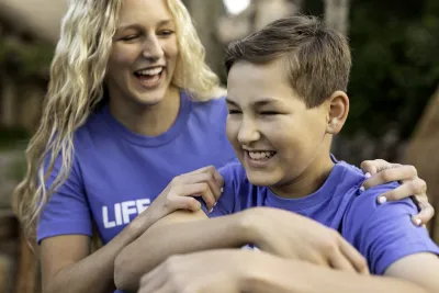 A boy and his mother smiling together while outside.