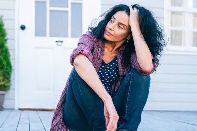 A woman sitting on the porch looking concerned.