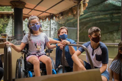 A young girl in a wheelchair and wearing a mask while riding Disney's Jungle Cruise ride.