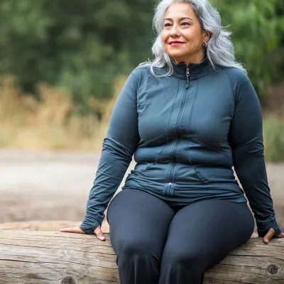 A mature woman sits outside on a log