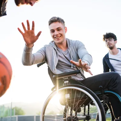 Older teens playing basketball one of which is in a wheelchair