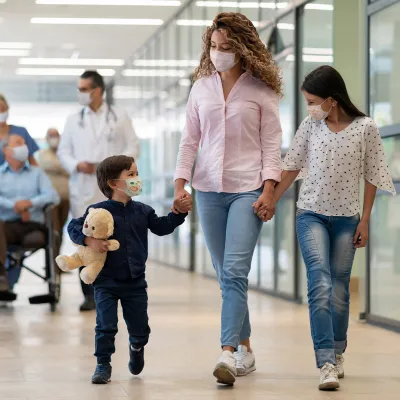A Mother and Her Two Children Walk Hand and Hand Through a Hospital Hallway