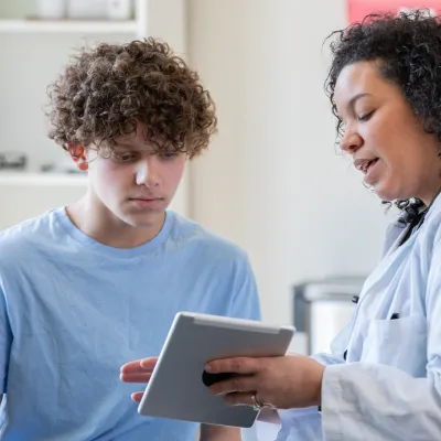 A Physician Goes Over a Teenager's Chart on a Tablet