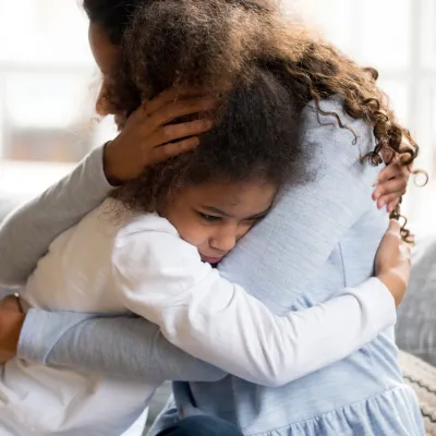 A Mother Hugs Her Sad Daughter on the Couch at Home.