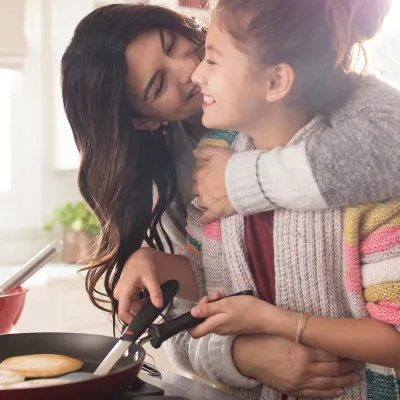 A woman hugging her daughter in the kitchen.