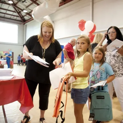 A woman giving school supplies to two little girls.