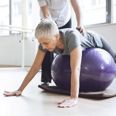 A Caucasian woman balances herself on an exercise ball.