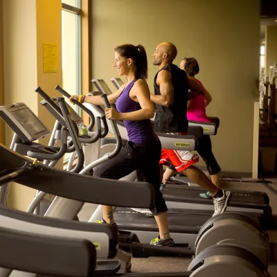 Three people running in different elliptical machines