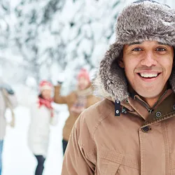 A group of people in snow, with a man at the forefront in focus in a brown jacket with a hod.