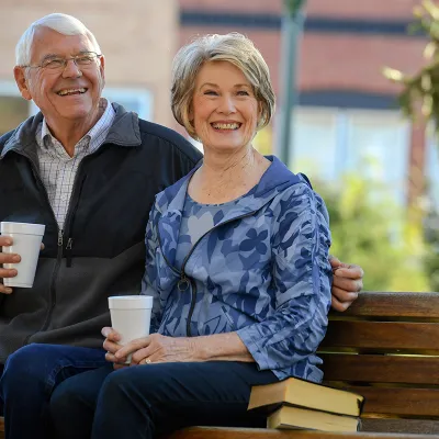 Elderly couple sitting on a park bench drinking coffee.
