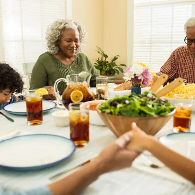 A family praying together while holding hands before eating lunch at home.