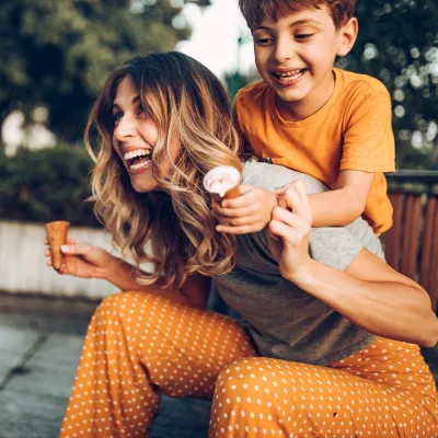 A Mother and Son Laugh and Play as They Eat Ice Cream Cones on a City Park Bench