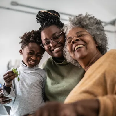 Grandmother, mother, and son smiling together while in the kitchen at home.
