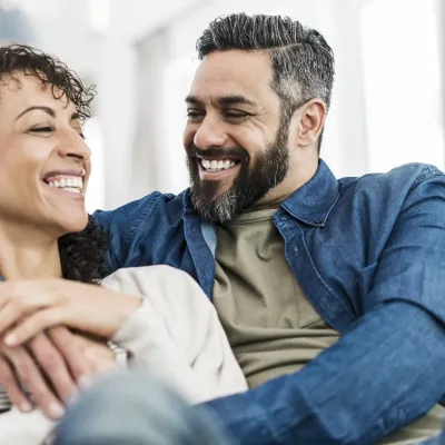 A couple laughing together on their couch at home.