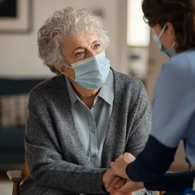 Hospice worker in mask, talking to elderly patient