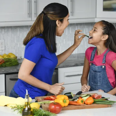 A mother and daughter snacking on vegetables.