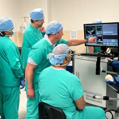 People in scrubs in operating room, pointing to screen.