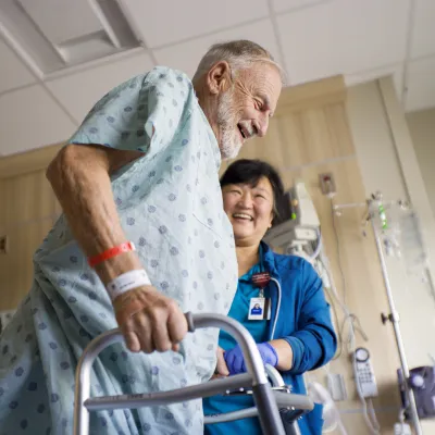 Older man using a walker with the help of a nurse