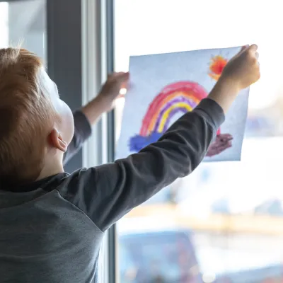 A child holding up a rainbow drawing.