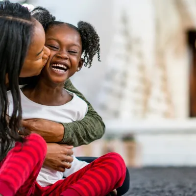 A mother hugging her daughter in front of the fireplace.