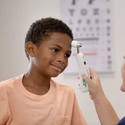 A Young Patient Smiles as a Primary Care+ Nurse Checks His Tempature