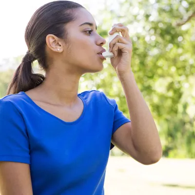 Young mixed-race woman using an asthma inhaler 