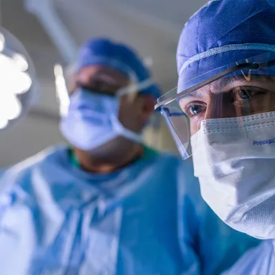 Close up of a surgeon in the foreground with another surgeon in the background in the operating room during a surgery.