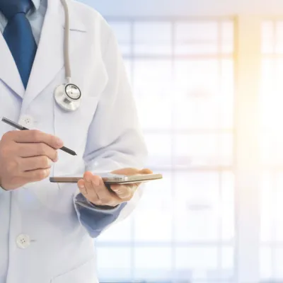 Physician holding a device and writing utensil in his hand