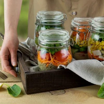 A person setting a tray of mason jars containing salads down on a table outdoors.