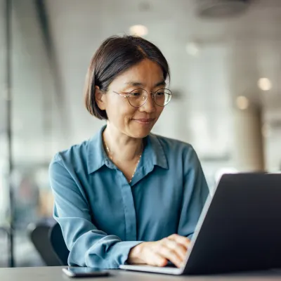 A woman sitting at a table using a laptop while indoors.