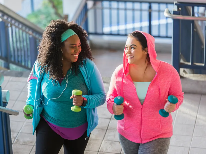 A Pair of Ladies, in Brightly Colored Clothing, Go Jogging in the City with Hand Weights.