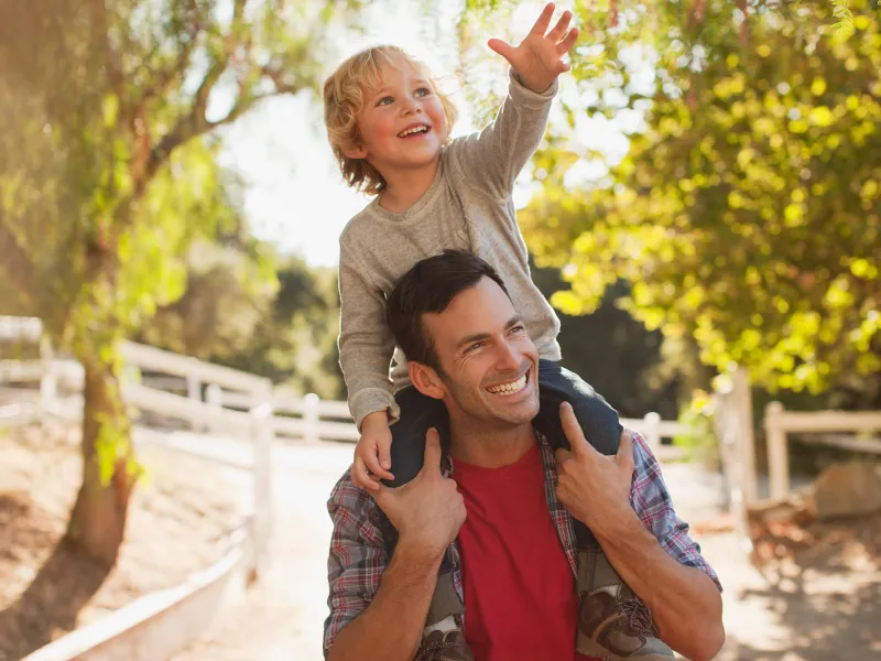 A Man Carrying His Son in a Playful Manner Over His Shoulders Through the Woods.