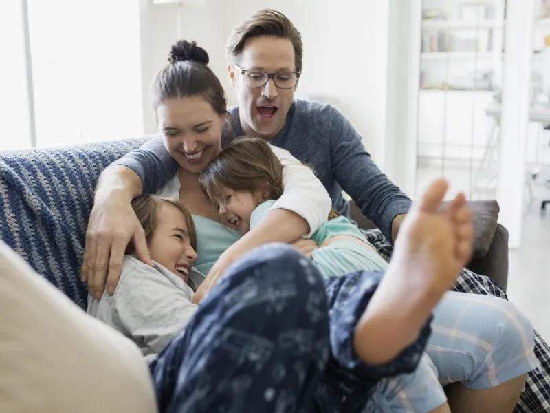 A Caucasian family laughs as they pile on the couch together.