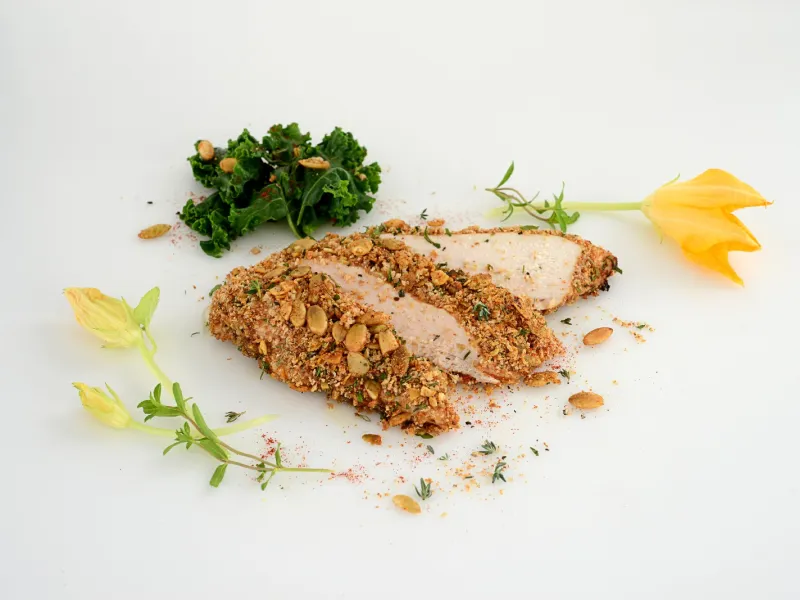 a serving of chicken, coated in a pumpkin seed crisp, sliced into three pieces