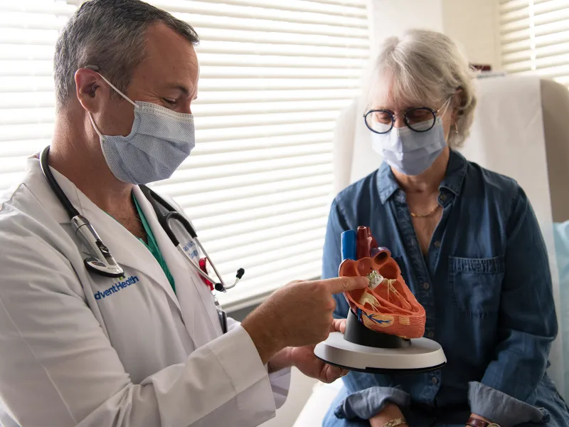 Doctor showing a woman patient a heart model while both wear masks.