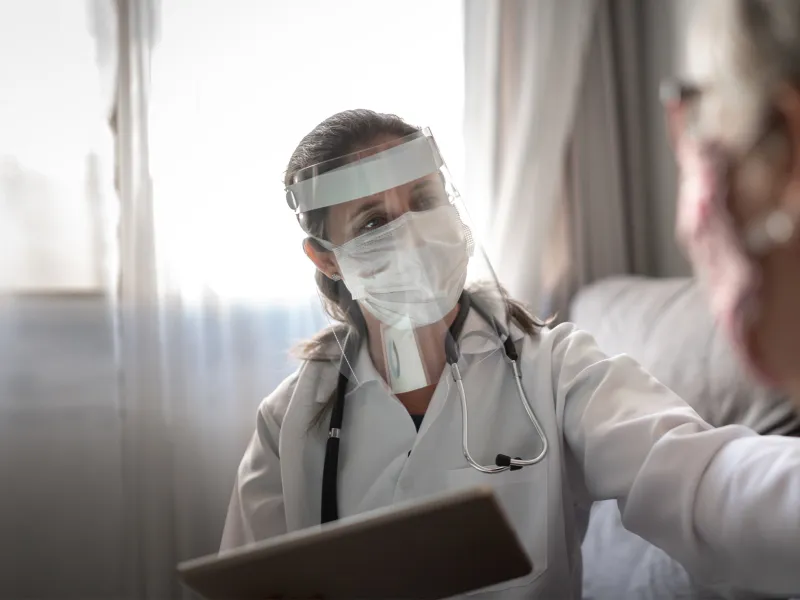 Doctor wearing PPE and talking with a patient that's wearing a mask.