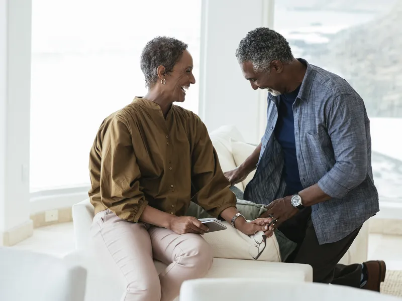 An African American couple smile and laugh on a couch in their home.