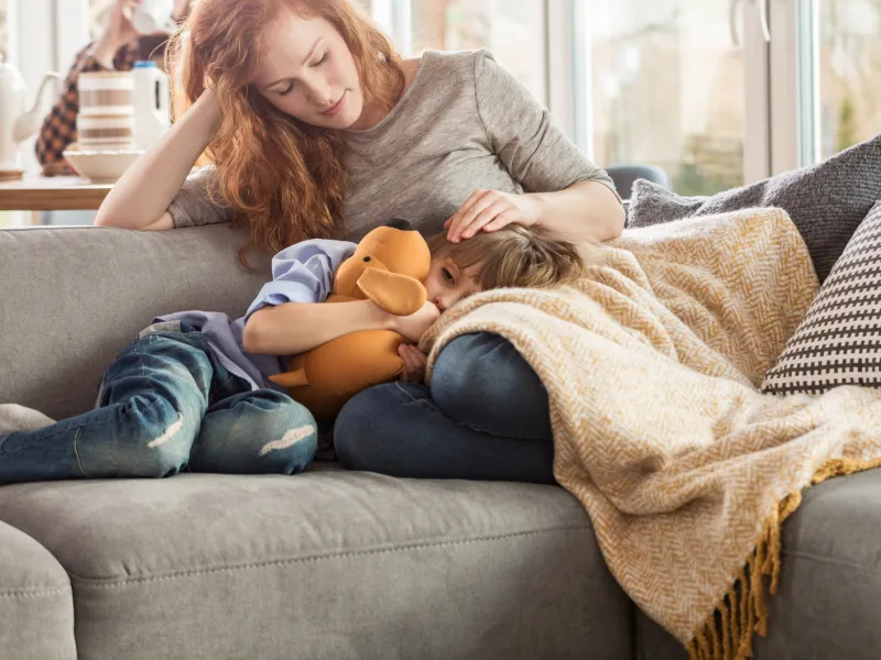 Sick child with mom on couch.