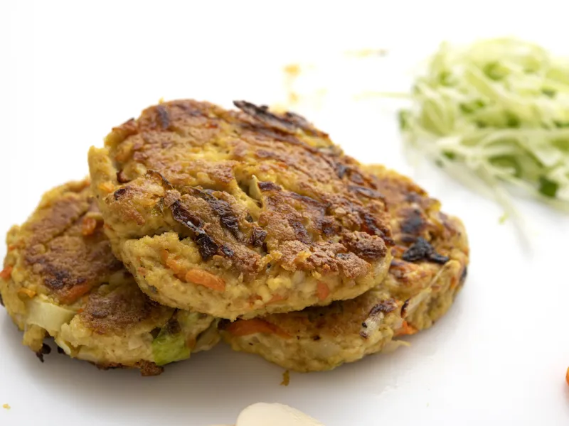 Three tofu yung patties on white surface with shredded zucchini garnish
