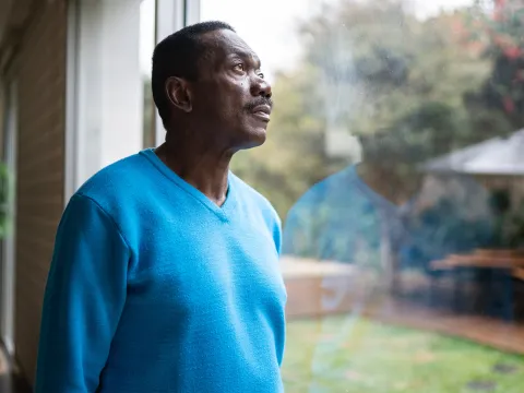 An African American Man Looks Out a Window into the Forest. 
