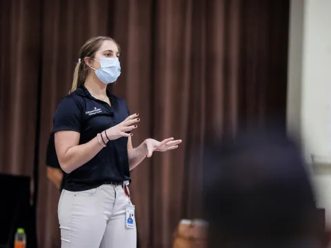 A masked woman on a stage giving a presentation
