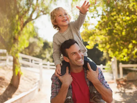 A Man Carrying His Son in a Playful Manner Over His Shoulders Through the Woods.