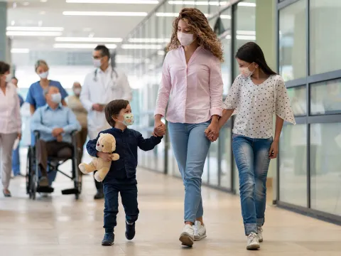 A Mother and Her Two Children Walk Hand and Hand Through a Hospital Hallway