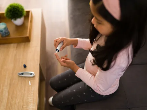 A little girl checking her sugar level using an at-home tester.
